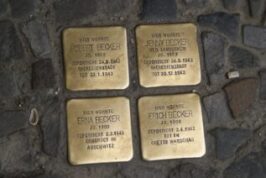 The image shows a "Stolperstein" or stumbling stone. This is a ten-centimetre concrete cube bearing a brass plate inscribed with the name and life dates of victims of Nazi extermination or persecution.